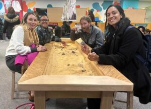 Group of young leaders sitting at sand table at science center and smiling at camera