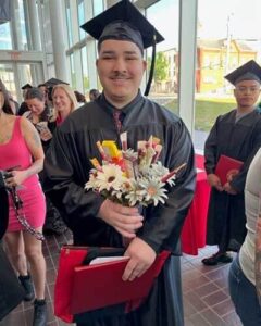 Young male holding bouquet of flowers smiling at camera in graduation cap and gown